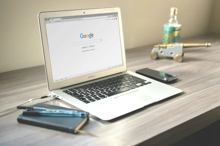 How to Earn Money Through Digital Marketing: A Complete Guide for Pakistan 3 A neat workspace featuring a laptop displaying Google search, a smartphone, and a notebook on a wooden desk.